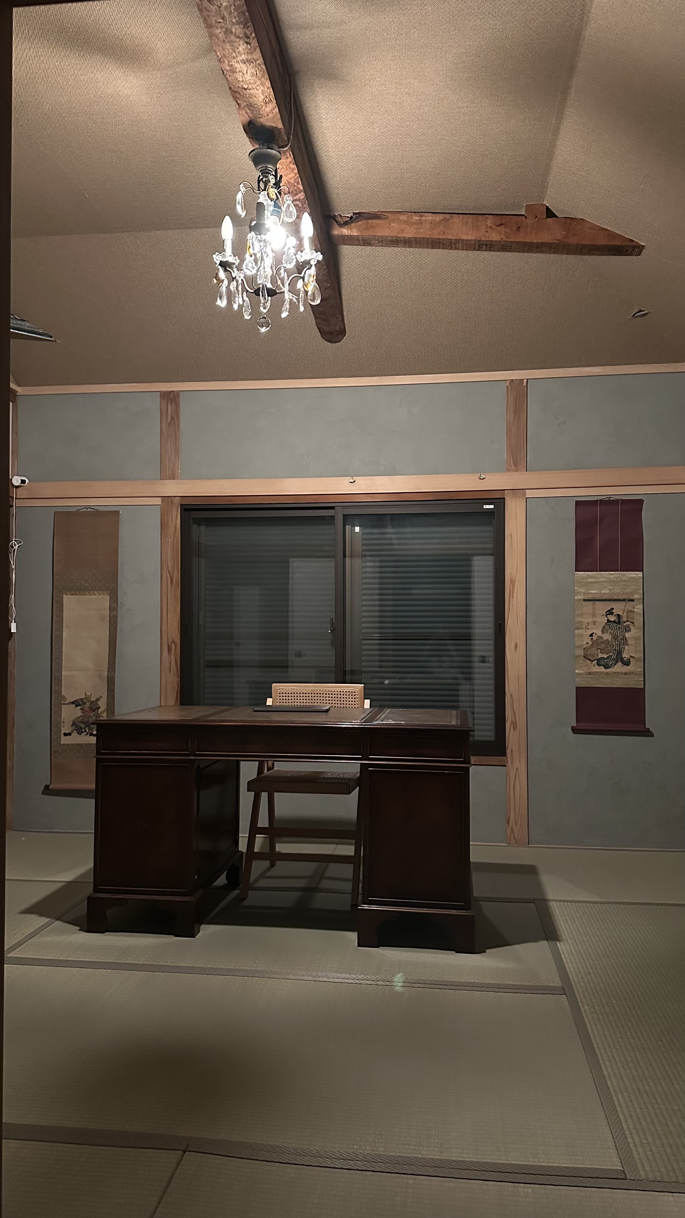 Traditional tatami room with wooden desk, hanging scrolls, and chandelier